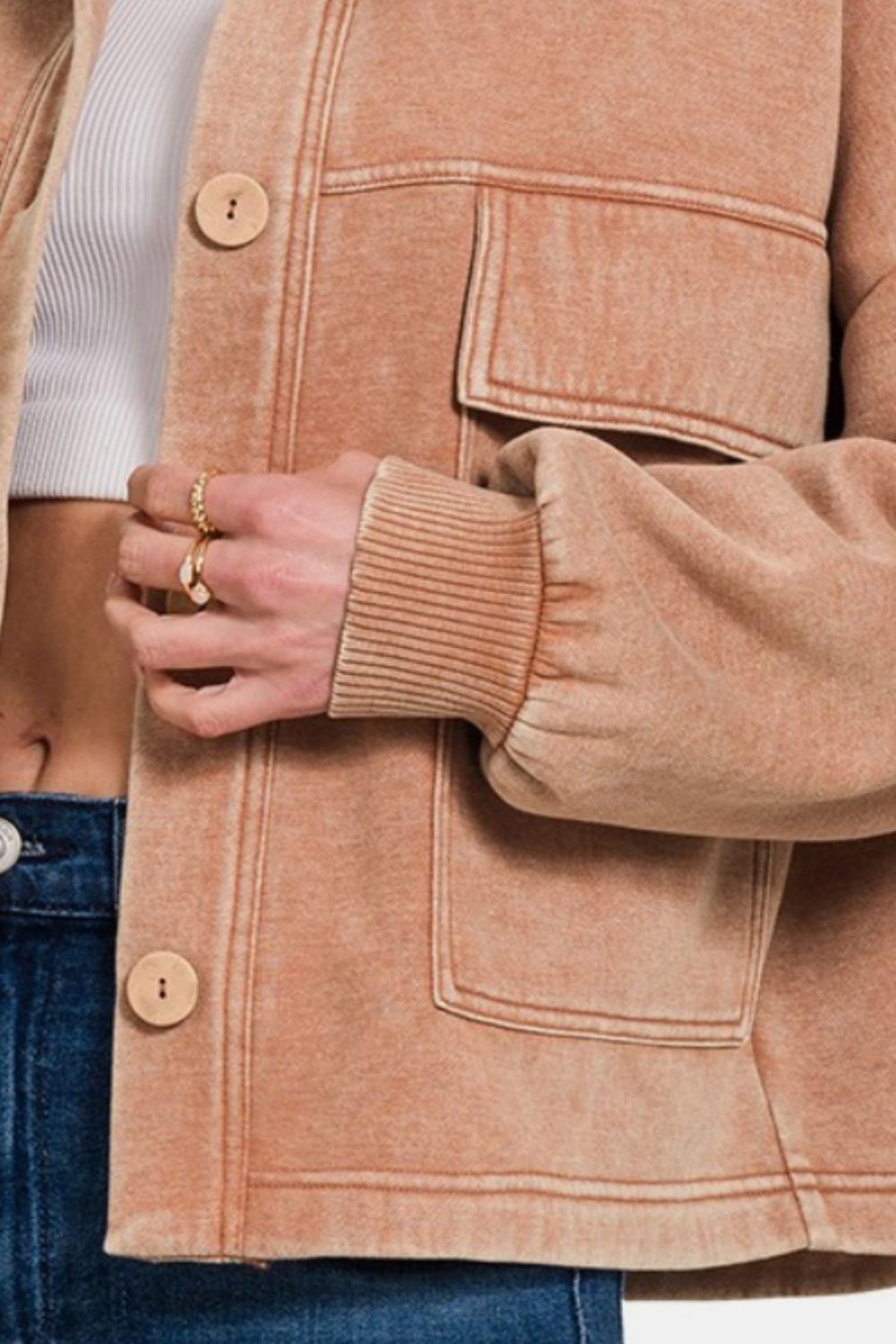 A person wearing the Zenana Wash Fleece Front Pocket Button Up Shacket in tan and blue jeans poses stylishly against a plain background.