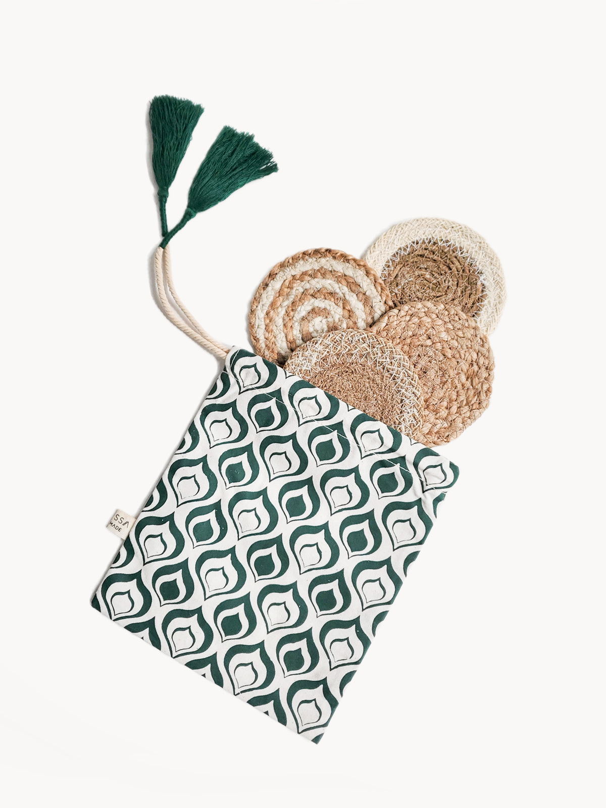 Introducing the Natural Coaster Gift Set with Green Pouch: a sustainable gift featuring a fabric pouch adorned in a green and white pattern, containing six round woven jute coasters. Delightful green tassels add an extra touch of charm, and each piece is skillfully crafted by fair trade artisans.