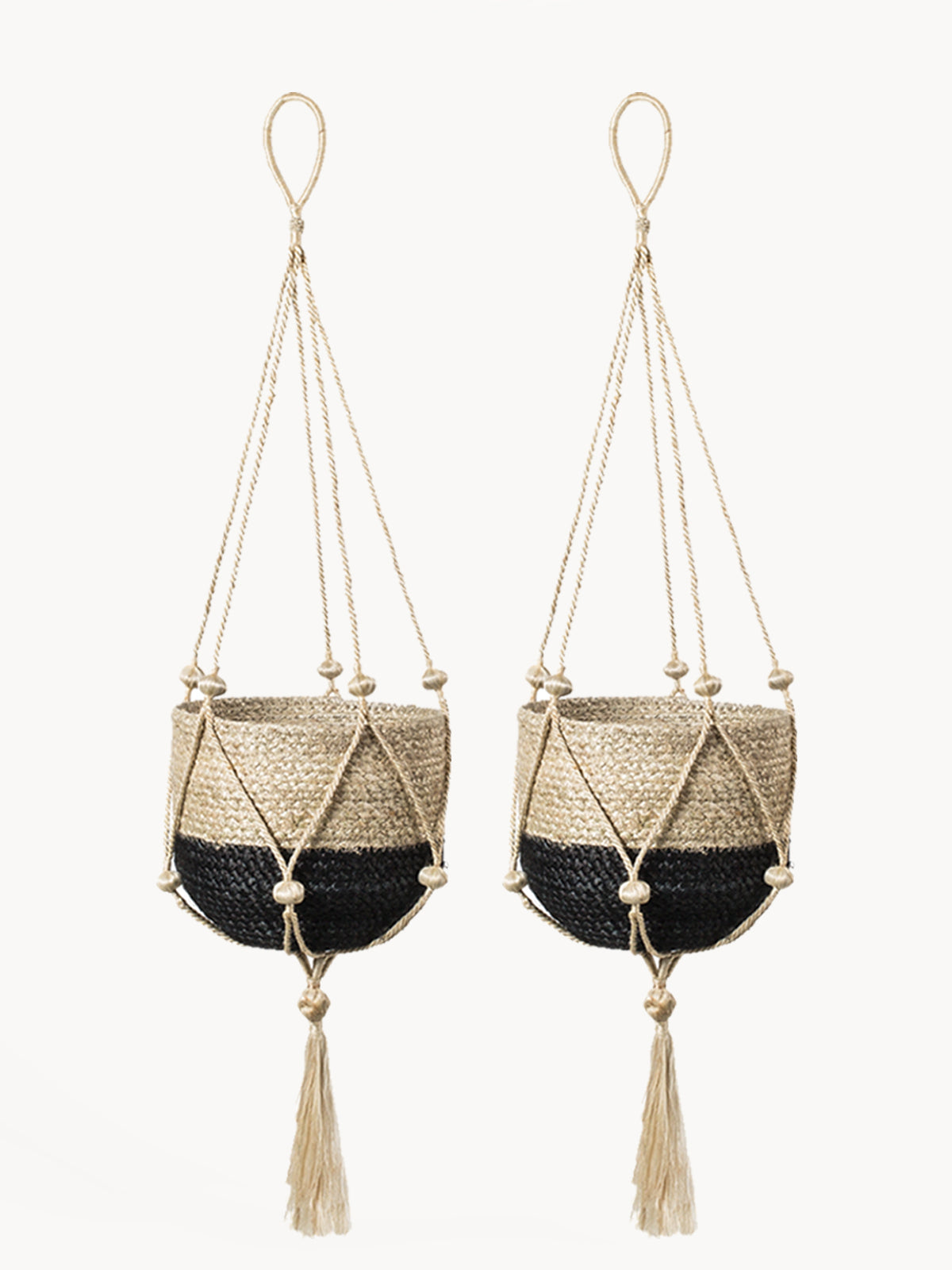 The Plant Hanger - Nadu features a woven basket with a black and natural fiber design, suspended by a handmade jute hanger adorned with braided and knotted ropes, complete with a tassel at the bottom.