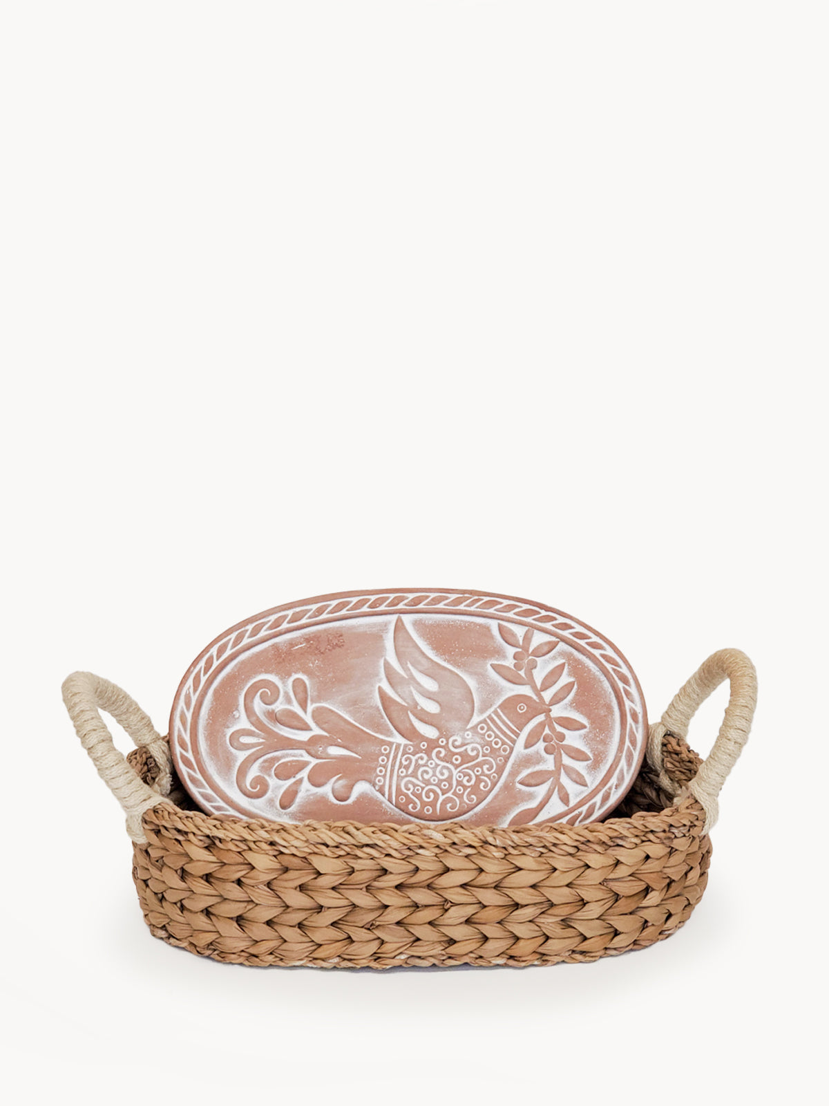 The Bird Oval Bread Warmer & Basket is an expertly crafted product, featuring an oval terracotta platter adorned with a white bird design, set within a handcrafted basket with two loop handles by Fair Trade artisans.