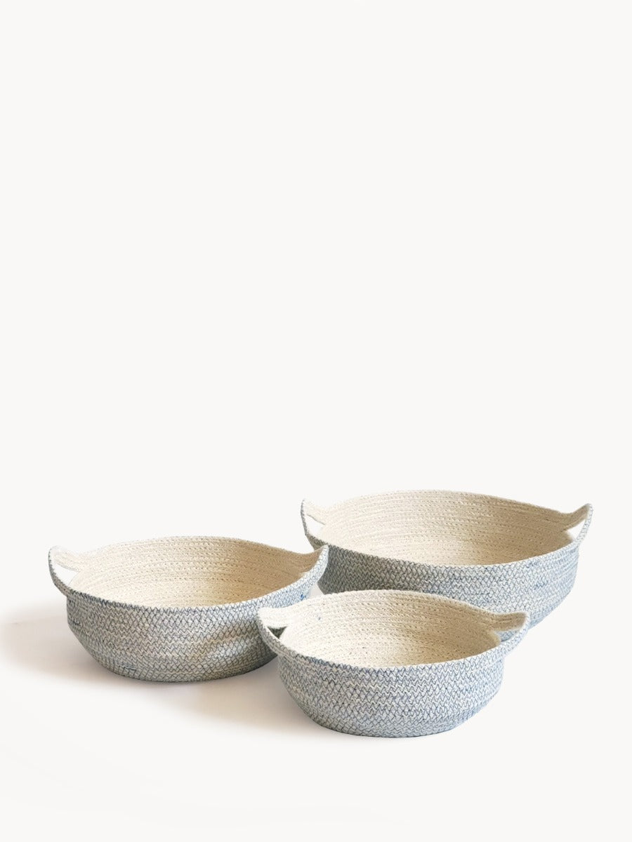 Three round, handwoven blue Amari fruit bowls are nested together. Crafted by Fair Trade artisans, these sustainably handmade pieces add a touch of elegance to any space.