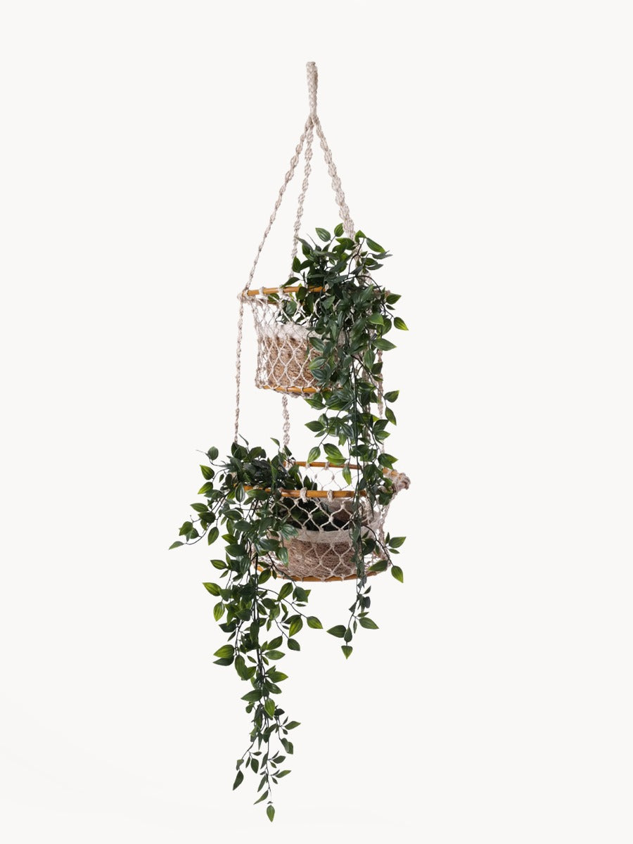 The Jhuri Double Hanging Basket is a macramé plant holder with two intricately woven baskets, each holding a lush green plant. Created by Fair Trade artisans, this piece showcases sustainably handmade craftsmanship and timeless elegance against a simple backdrop.