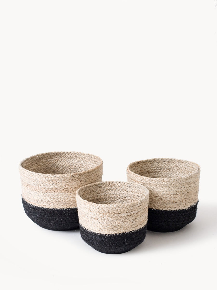 Three Naiya Bin baskets, handwoven by Fair Trade artisans with varying sizes and featuring natural upper halves and black lower halves, are arranged side by side against a light background.