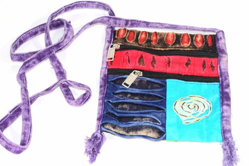 The Spiral Cross Body Patchwork Passport Bag features a vibrant hippie style with red, purple, blue, and green patterns. Handmade from cotton, it comes with multiple zippers and an adjustable strap, adorned with a charming flower design on the lower right corner.