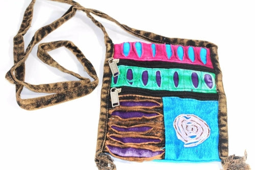 The Spiral Cross Body Patchwork Passport Bag features a vibrant hippie style with red, purple, blue, and green patterns. Handmade from cotton, it comes with multiple zippers and an adjustable strap, adorned with a charming flower design on the lower right corner.