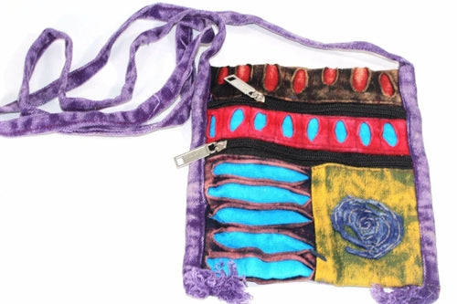 The Spiral Cross Body Patchwork Passport Bag features a vibrant hippie style with red, purple, blue, and green patterns. Handmade from cotton, it comes with multiple zippers and an adjustable strap, adorned with a charming flower design on the lower right corner.