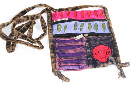 The Spiral Cross Body Patchwork Passport Bag features a vibrant hippie style with red, purple, blue, and green patterns. Handmade from cotton, it comes with multiple zippers and an adjustable strap, adorned with a charming flower design on the lower right corner.