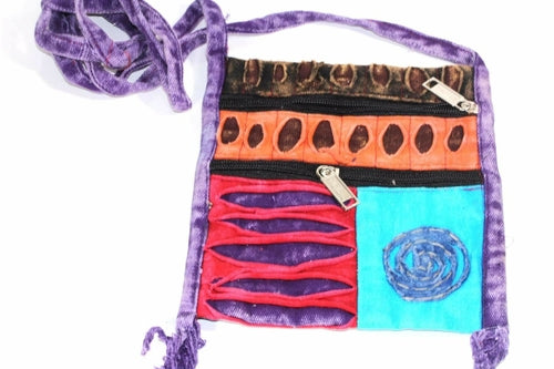 The Spiral Cross Body Patchwork Passport Bag features a vibrant hippie style with red, purple, blue, and green patterns. Handmade from cotton, it comes with multiple zippers and an adjustable strap, adorned with a charming flower design on the lower right corner.
