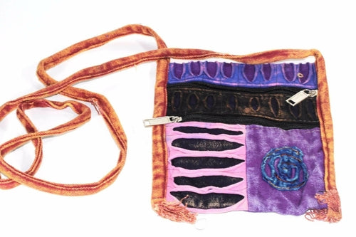 The Spiral Cross Body Patchwork Passport Bag features a vibrant hippie style with red, purple, blue, and green patterns. Handmade from cotton, it comes with multiple zippers and an adjustable strap, adorned with a charming flower design on the lower right corner.
