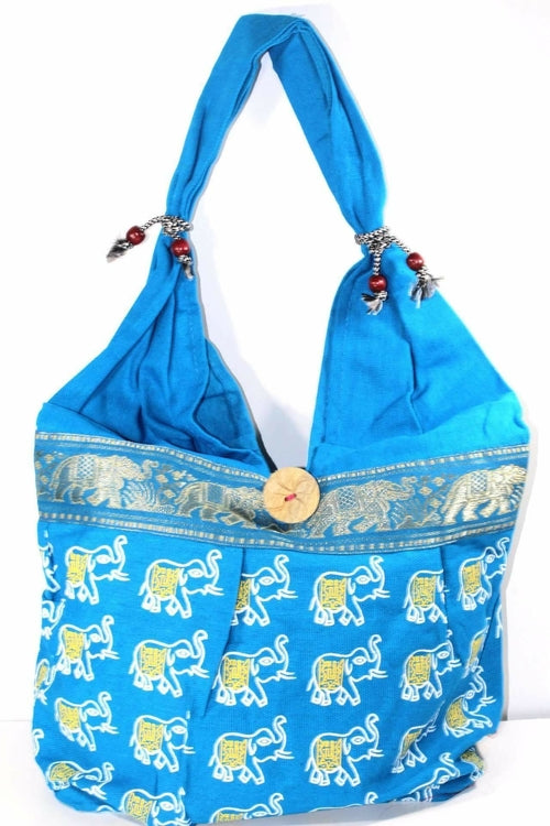 The Elephant Jhola Bag is a handmade cotton tote featuring a vibrant yellow elephant print, colorful jacquard trim, decorative tassels, and a wooden button closure—ideal as a stylish travel accessory.