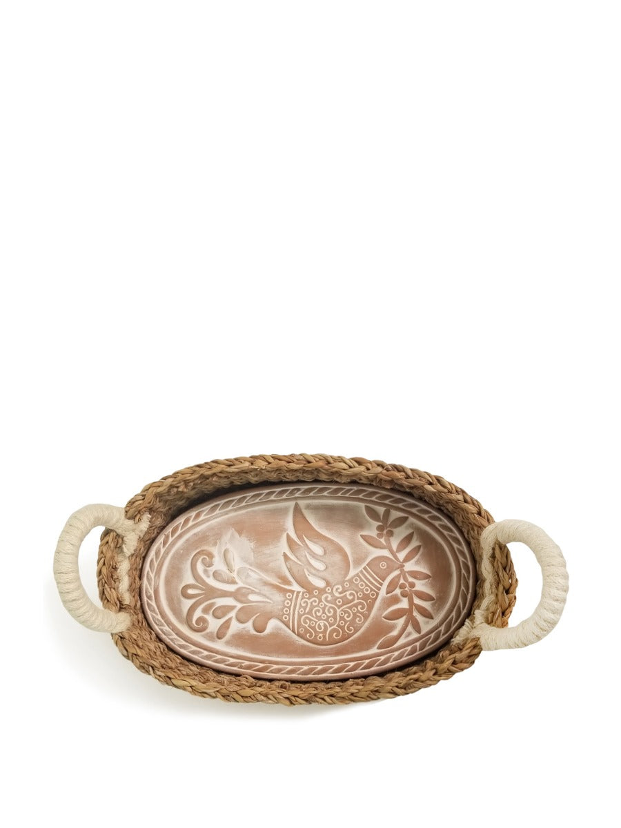 The Bird Oval Bread Warmer & Basket is an expertly crafted product, featuring an oval terracotta platter adorned with a white bird design, set within a handcrafted basket with two loop handles by Fair Trade artisans.