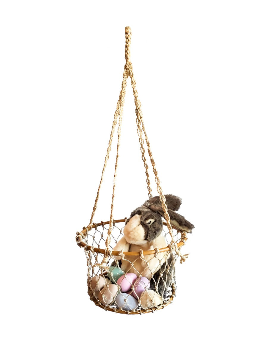 The Jhuri Single Hanging Basket, crafted from natural jute by Fair Trade artisans, cradles a lush plant with trailing green leaves against a plain white background, beautifully combining elegance and sustainability.