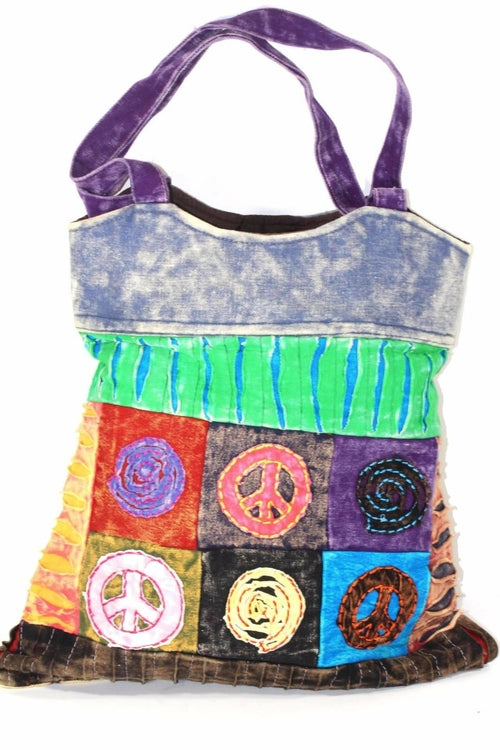 The Peace & Om Patchwork Jhola Carry Bag, featuring green handles, presents spiritual symbols like peace and Om in multicolored embroidered squares through its vibrant handmade design.