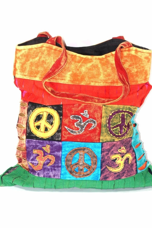 The Peace & Om Patchwork Jhola Carry Bag, featuring green handles, presents spiritual symbols like peace and Om in multicolored embroidered squares through its vibrant handmade design.