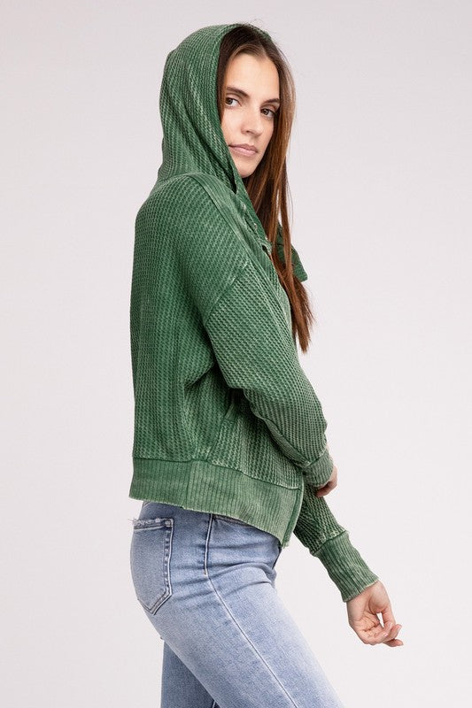 Woman in a Acid Wash Cotton Waffle Hooded Zip-Up Jacket with pockets and black pants, smiling and posing with hands on hips, against a light gray background.
