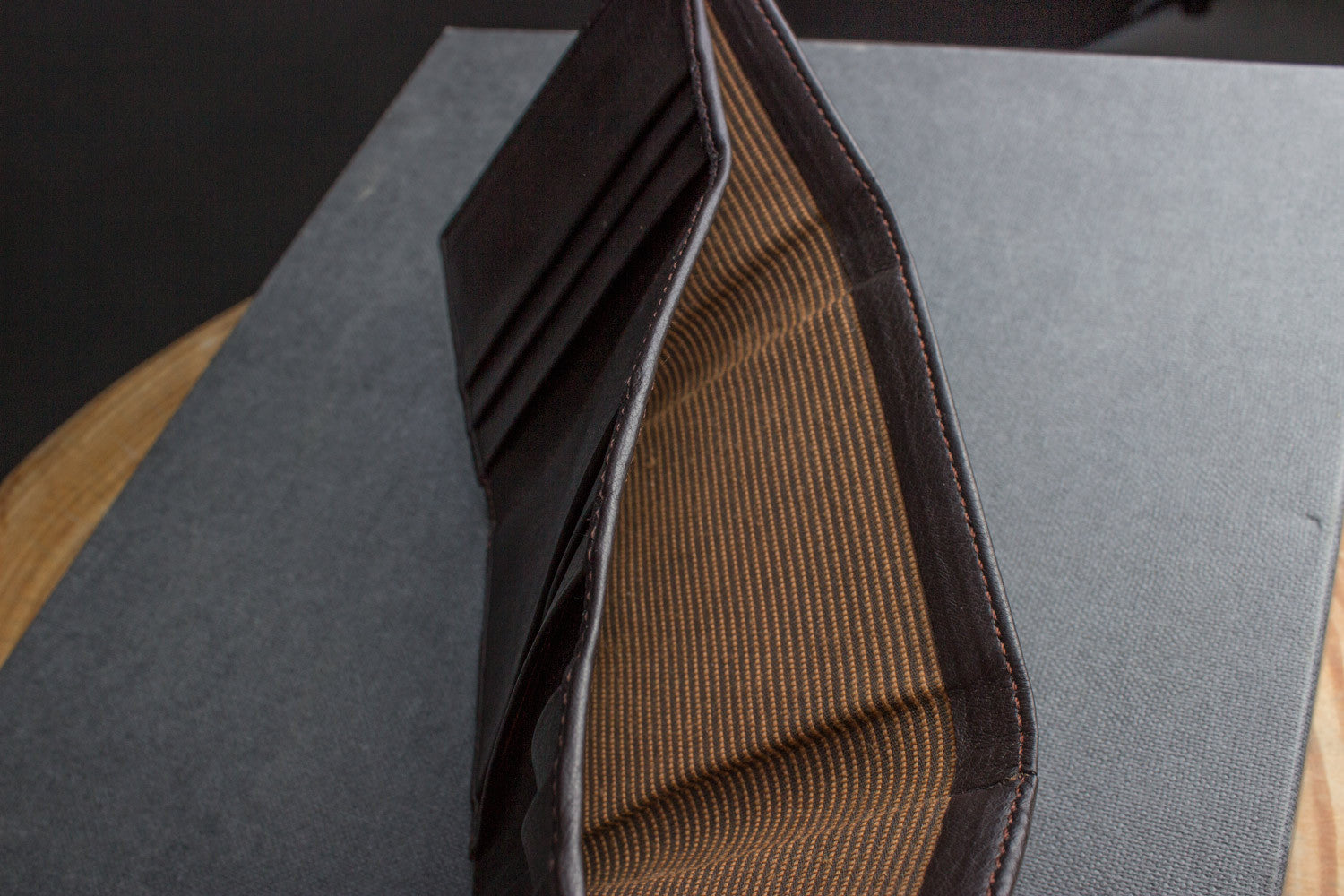 A Trifold Wallet made from full grain cowhide leather holds cash, a card, and has a visible ID section on top of a closed red notebook.