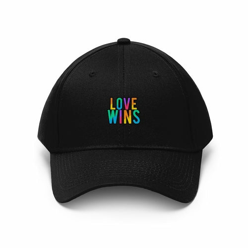 A bearded man wears the Rainbow Love Wins Unisex Twill Cap adorned with the phrase "Rainbow Love Wins" in vibrant colors, along with a gray sweatshirt, as he gazes into the distance against a simple backdrop.
