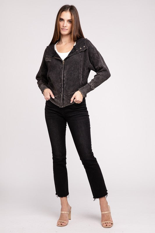 Woman in a Acid Wash Cotton Waffle Hooded Zip-Up Jacket with pockets and black pants, smiling and posing with hands on hips, against a light gray background.