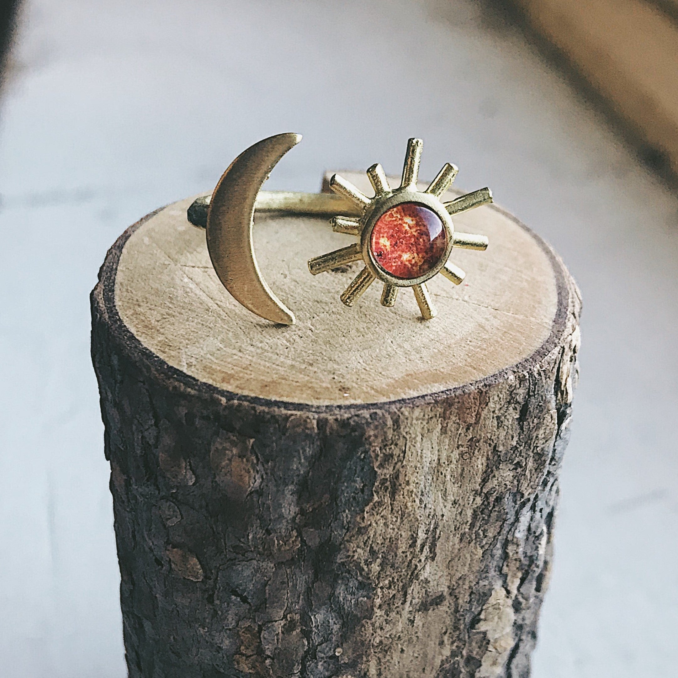 A hand adorned with the Sun and Moon Sculptural Statement Ring, showcasing a celestial design of a crescent moon and sun paired with a captivating red-orange gemstone. This adjustable ring beautifully captures the enchanting dance of day and night.