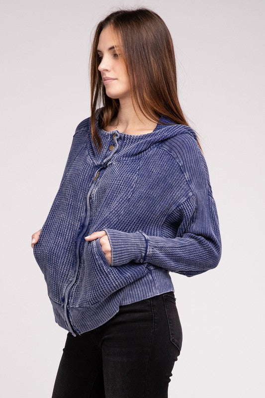 Woman in a Acid Wash Cotton Waffle Hooded Zip-Up Jacket with pockets and black pants, smiling and posing with hands on hips, against a light gray background.