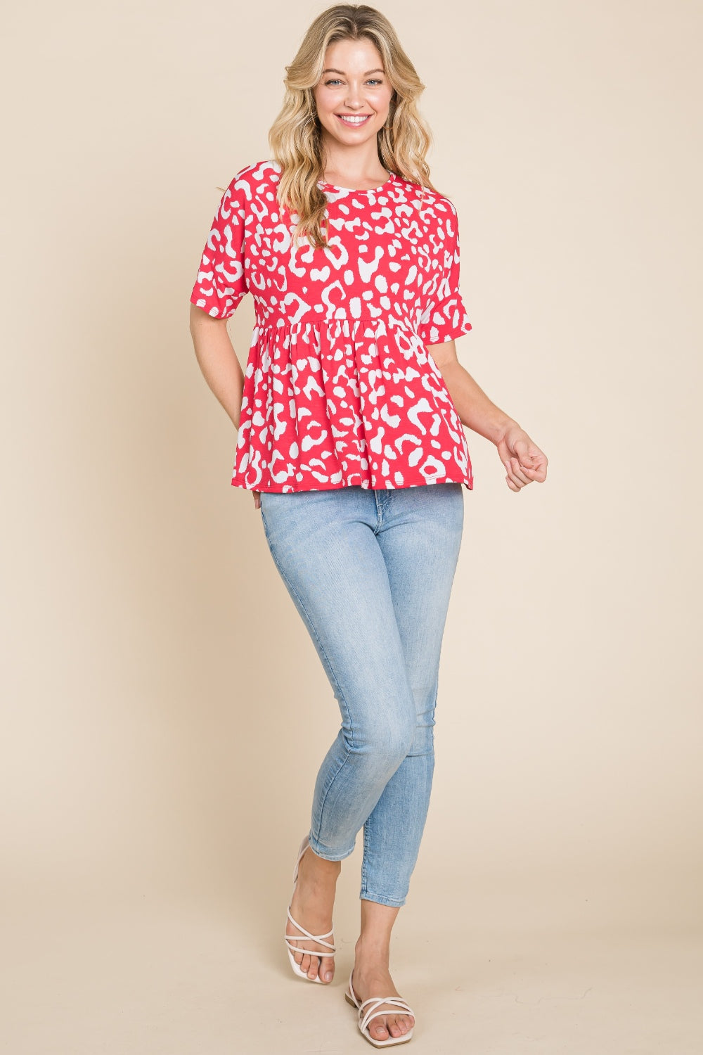 A person in a red and white BOMBOM Leopard Peplum Babydoll Blouse and blue jeans stands against a beige background.