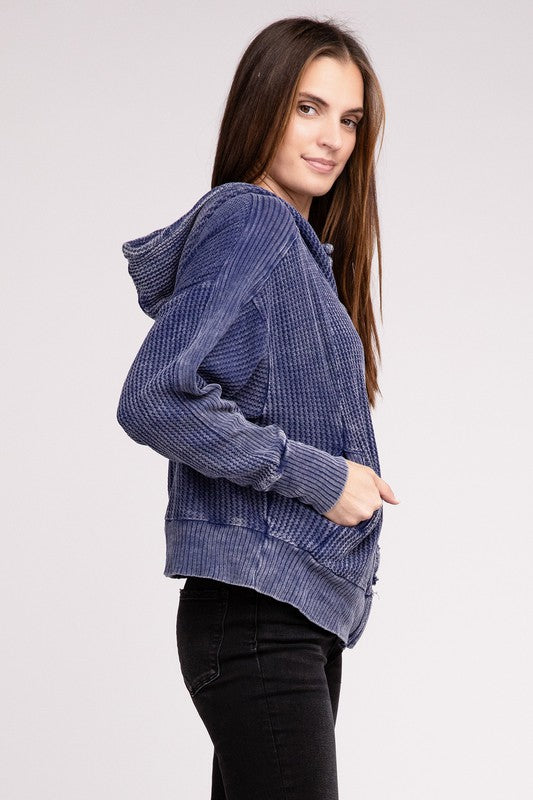 Woman in a Acid Wash Cotton Waffle Hooded Zip-Up Jacket with pockets and black pants, smiling and posing with hands on hips, against a light gray background.