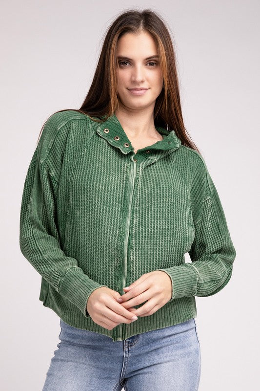 Woman in a Acid Wash Cotton Waffle Hooded Zip-Up Jacket with pockets and black pants, smiling and posing with hands on hips, against a light gray background.