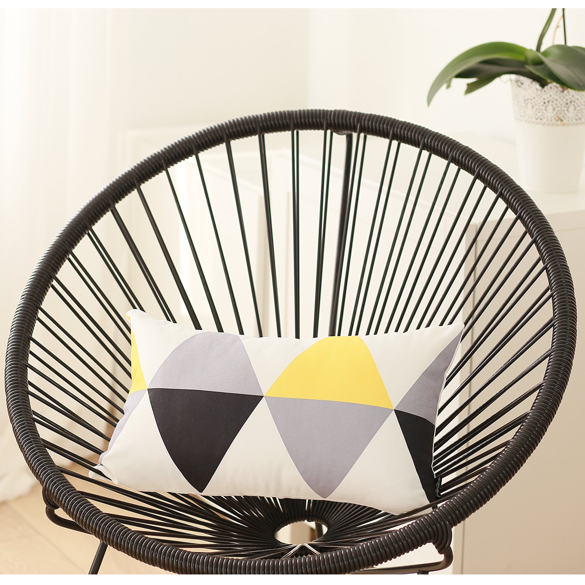A yellow sofa, accessorized with two Scandi Yellow Gray Modern Lumbar Throw Pillow Covers, certified by OEKO-TEX Standard 100 and featuring a geometric pattern, is positioned beside a green potted plant and illuminated by natural light from a nearby window.