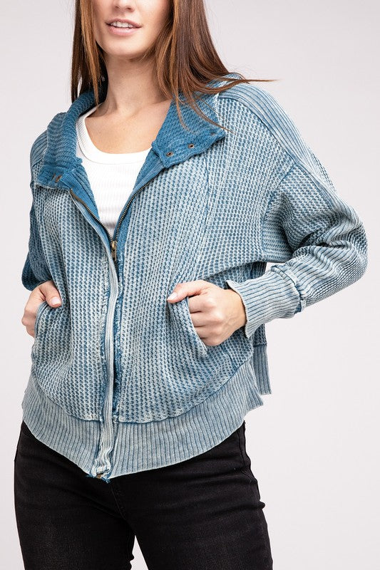 Woman in a Acid Wash Cotton Waffle Hooded Zip-Up Jacket with pockets and black pants, smiling and posing with hands on hips, against a light gray background.