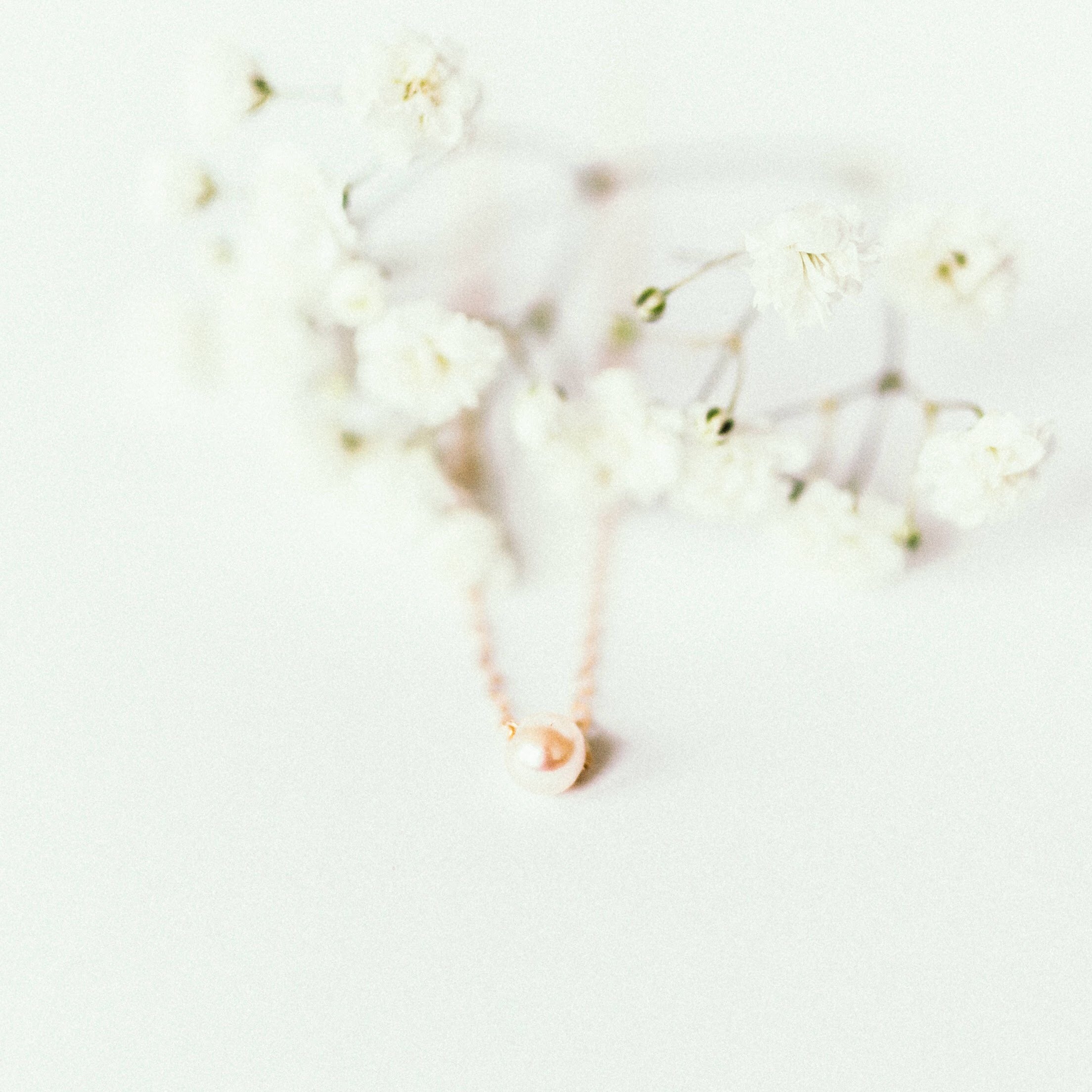 The Malaya Necklace, featuring a single small Philippine freshwater pearl pendant, is elegantly displayed on a white surface with its delicate 14k-gold filled chain.