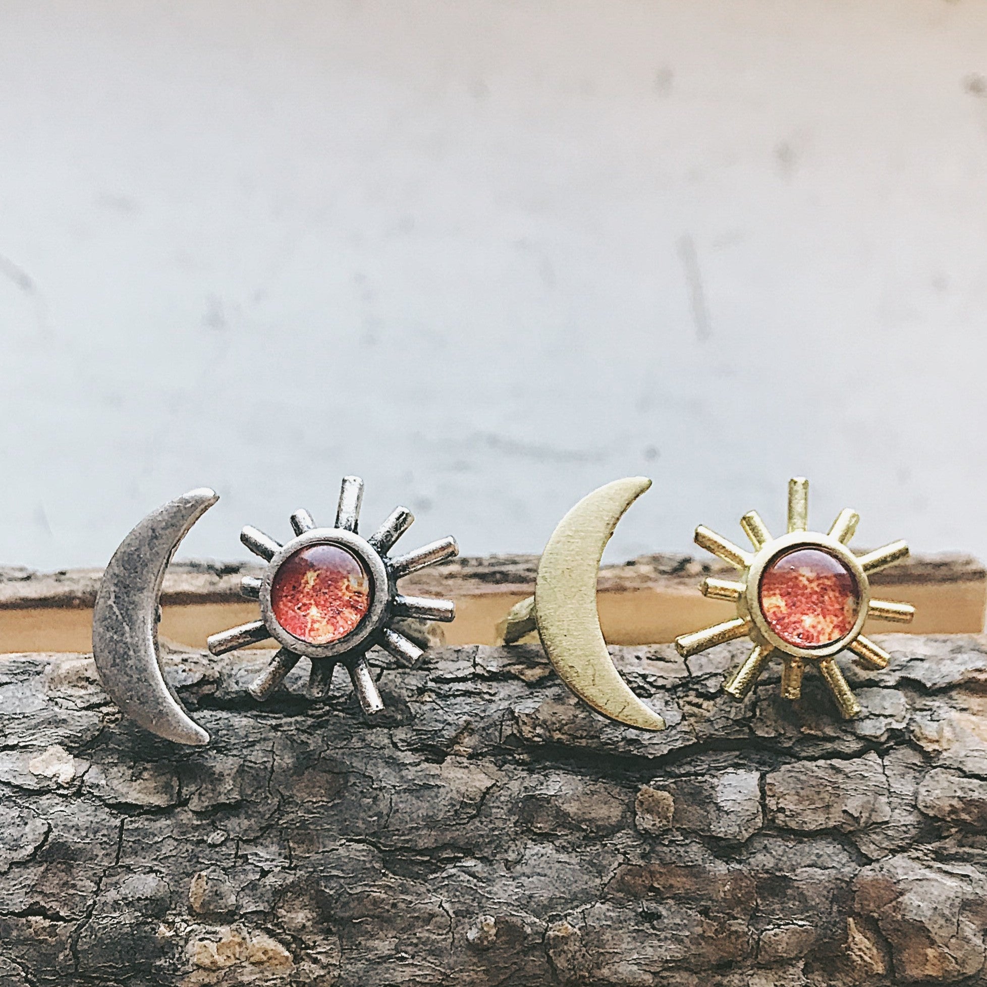 A hand adorned with the Sun and Moon Sculptural Statement Ring, showcasing a celestial design of a crescent moon and sun paired with a captivating red-orange gemstone. This adjustable ring beautifully captures the enchanting dance of day and night.