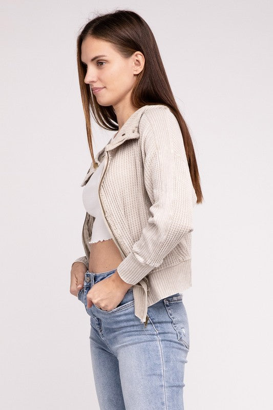Woman in a Acid Wash Cotton Waffle Hooded Zip-Up Jacket with pockets and black pants, smiling and posing with hands on hips, against a light gray background.