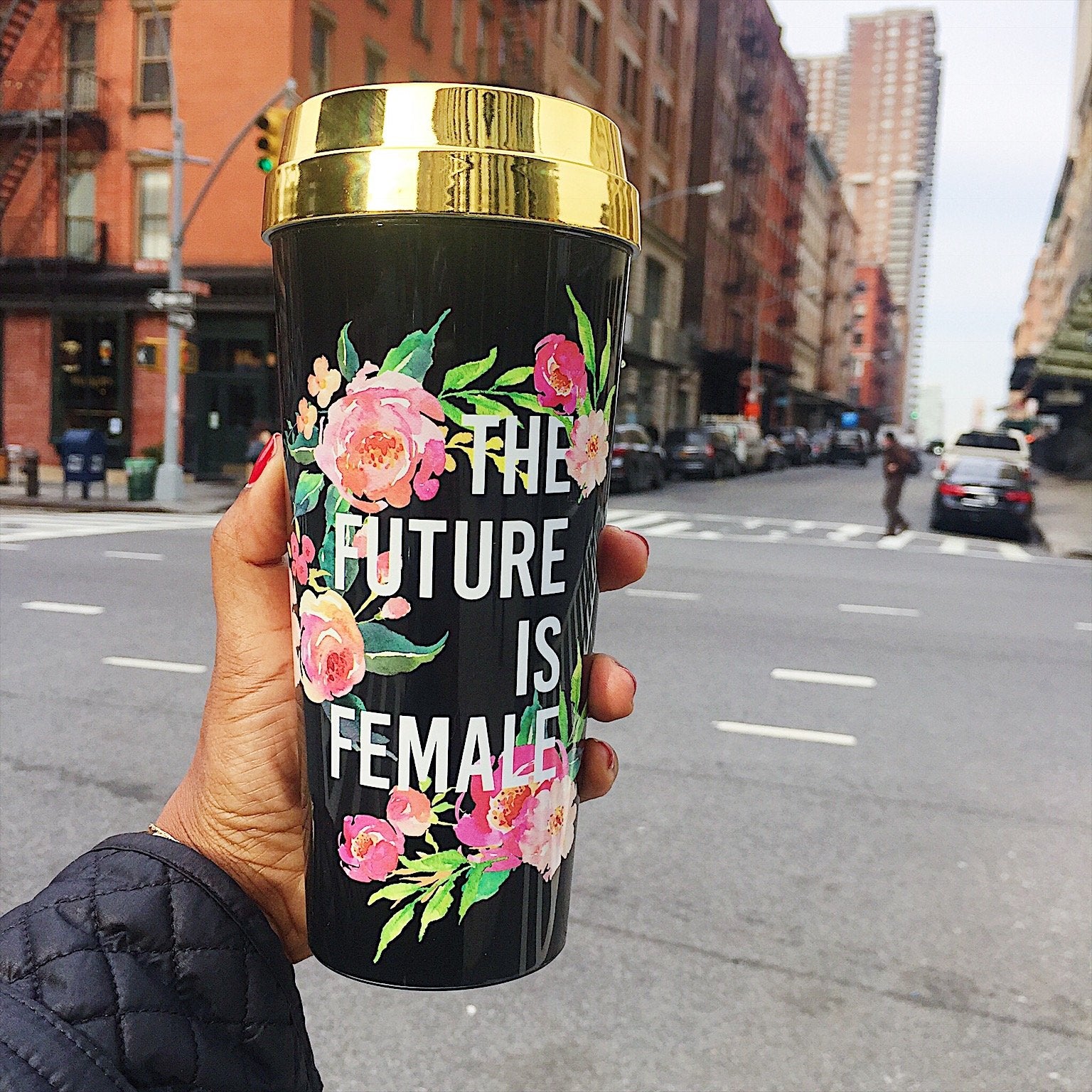 The travel mug, named "The Future Is Female," features elegant floral designs with a black body and a gold lid, prominently displaying the bold white phrase "The Future is Female," making it an ideal choice for those who support girl power and feminism.