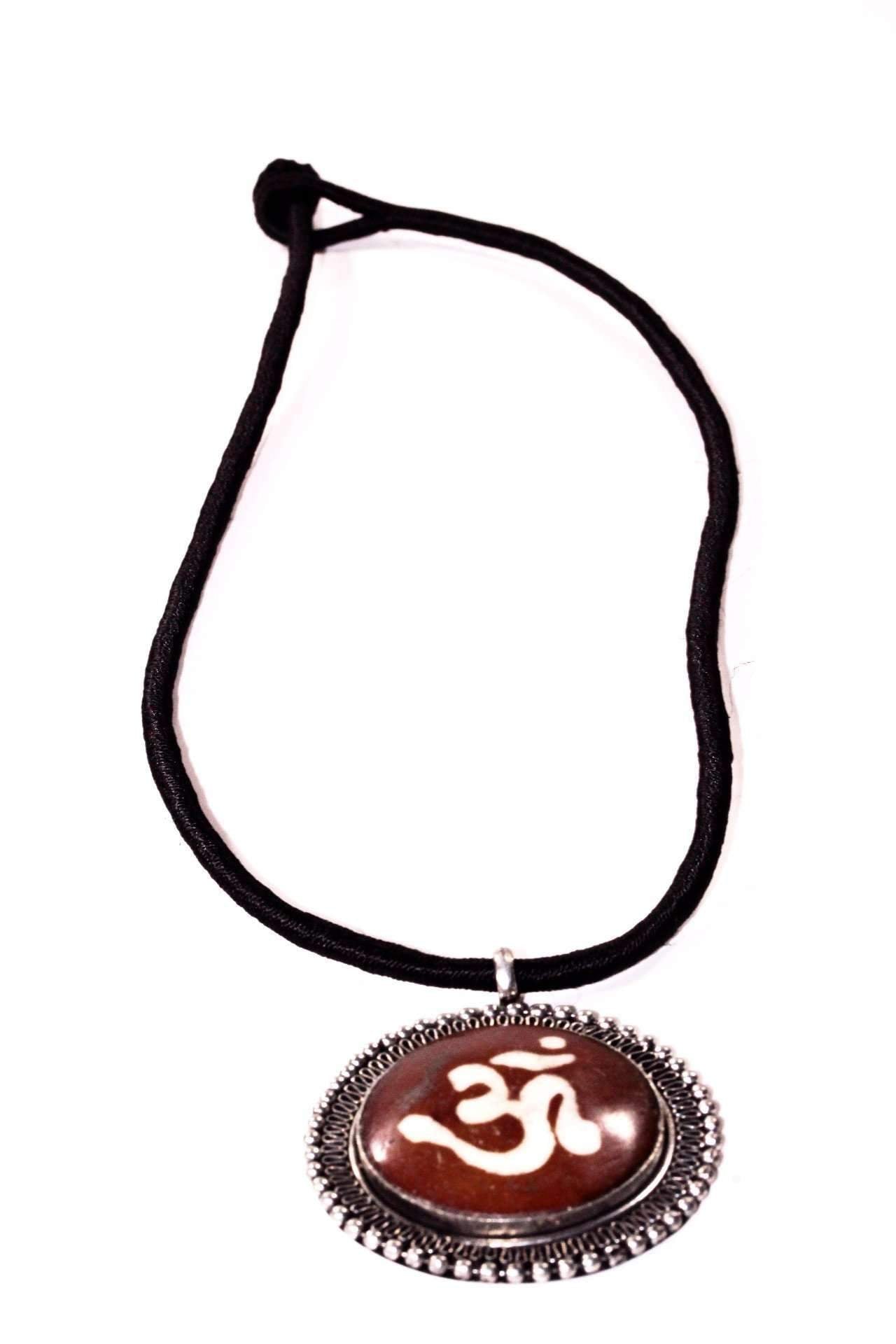 The Auspicious Om Spiritual Necklace, with a black cord and a round pendant featuring an Om symbol on a brown background framed by a decorative silver border, embodies boho-chic elegance.