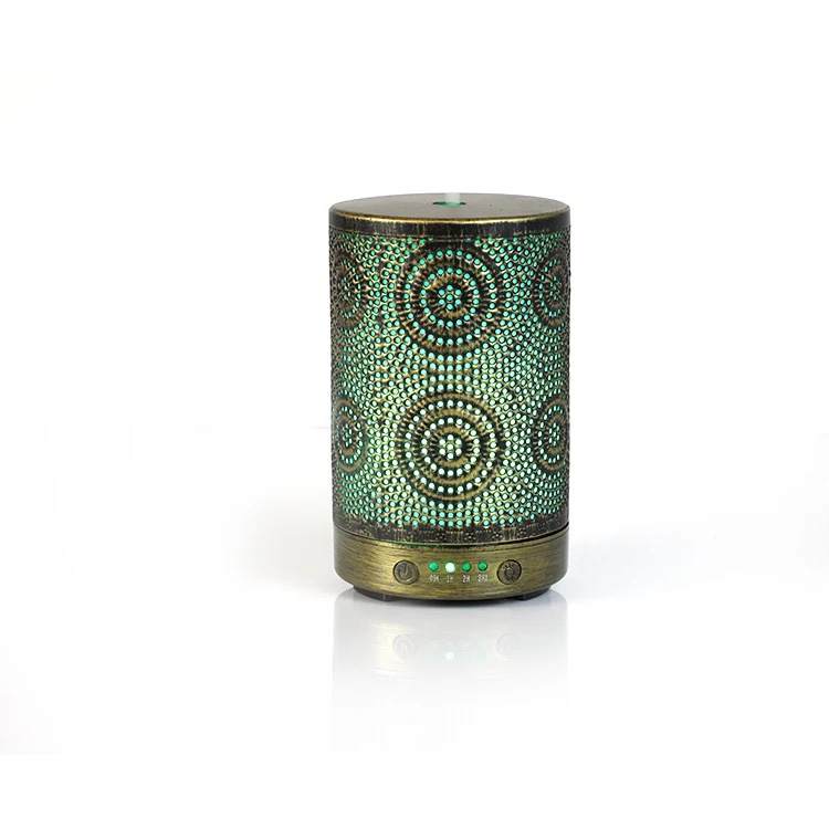 A chic Color Changing Aromatherapy Oil Diffuser with a floral motif rests on a wooden table, softly releasing mist enhanced with essential oils. In the background, a vase displays vibrant flowers, crafting an ideal aromatherapy atmosphere.