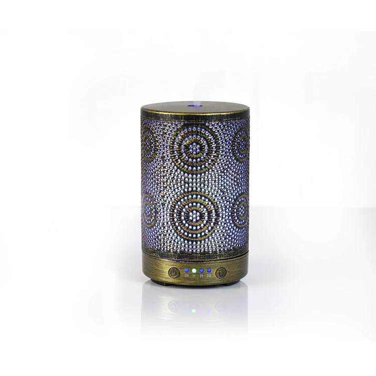 A chic Color Changing Aromatherapy Oil Diffuser with a floral motif rests on a wooden table, softly releasing mist enhanced with essential oils. In the background, a vase displays vibrant flowers, crafting an ideal aromatherapy atmosphere.