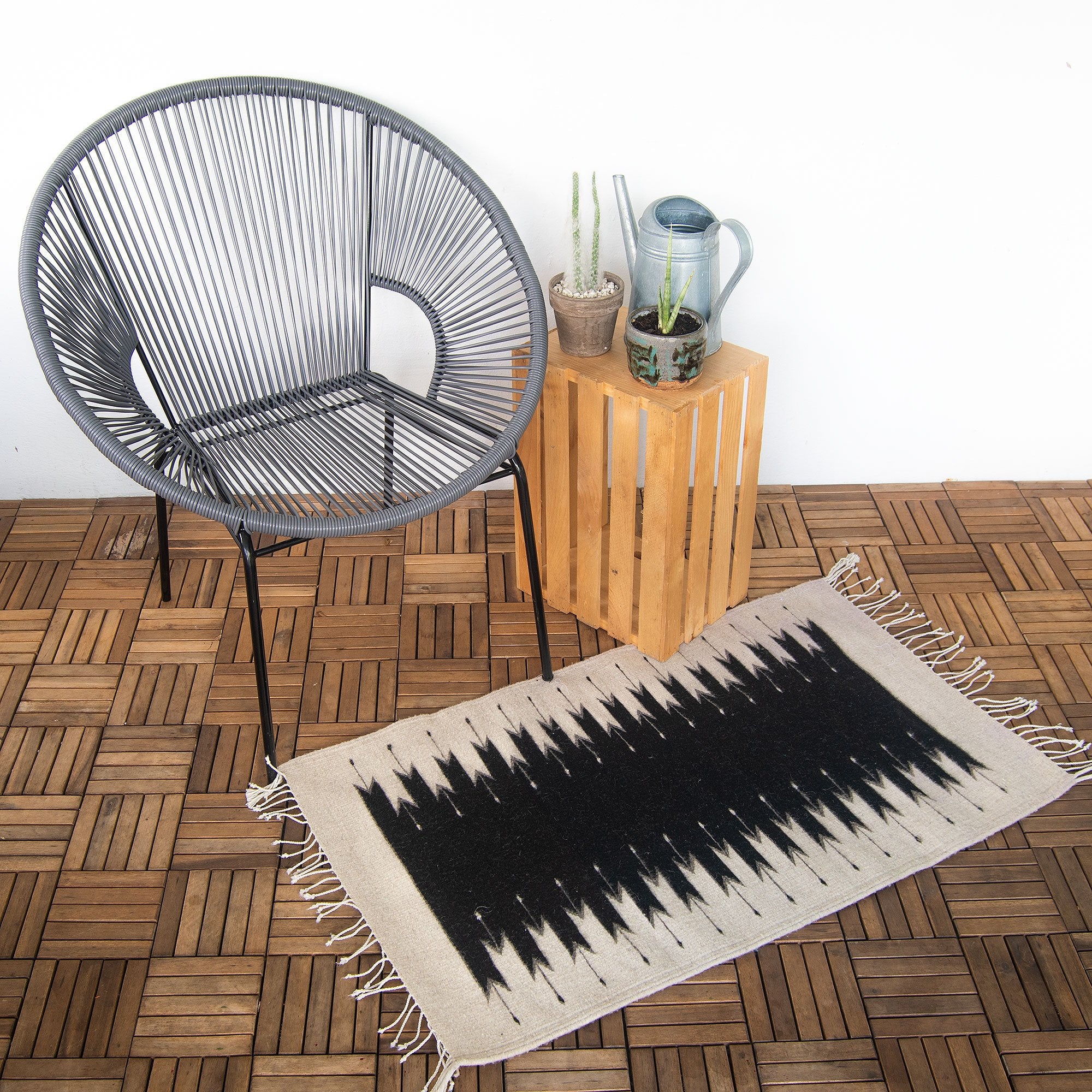 A mid-century modern leather armchair beside a white brick fireplace, with a Beleroó Handmade Southwestern Style Rug. Lightling Pattern in front and a metal watering can on the side.