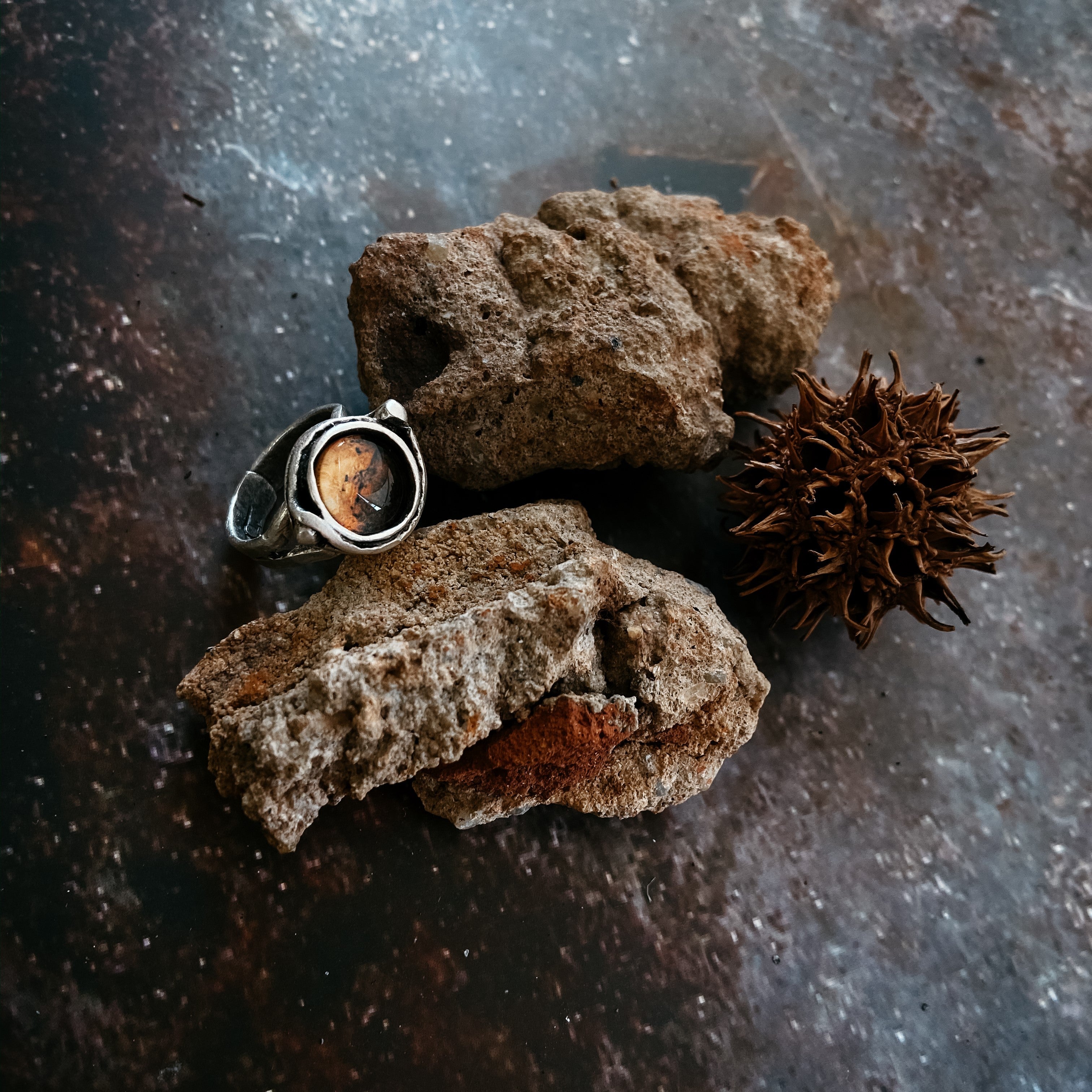 A hand wears the Mars and Moons Ring, featuring a silver tone with a spherical, galaxy-like design reminiscent of space exploration jewelry, set against a starry background.
