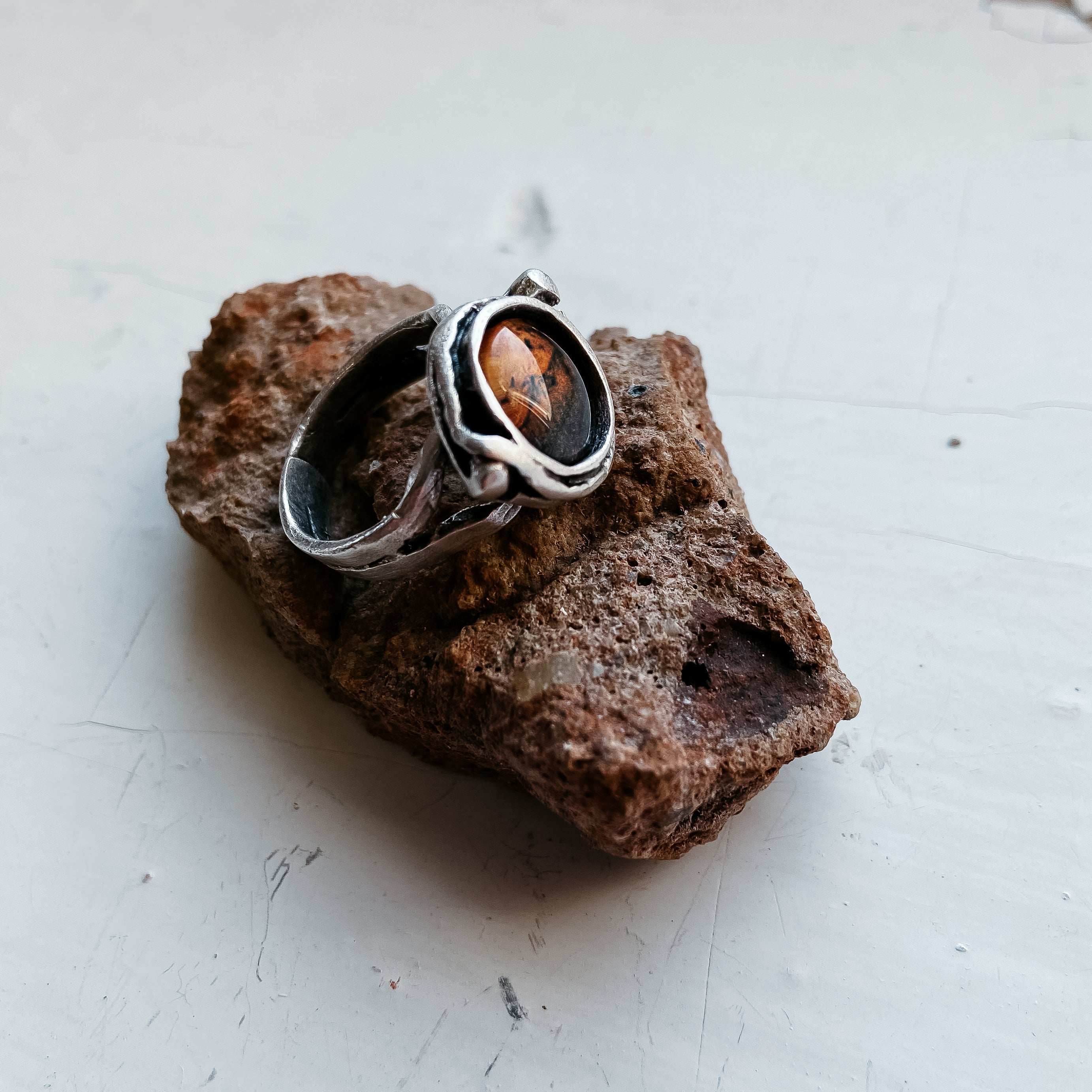 A hand wears the Mars and Moons Ring, featuring a silver tone with a spherical, galaxy-like design reminiscent of space exploration jewelry, set against a starry background.