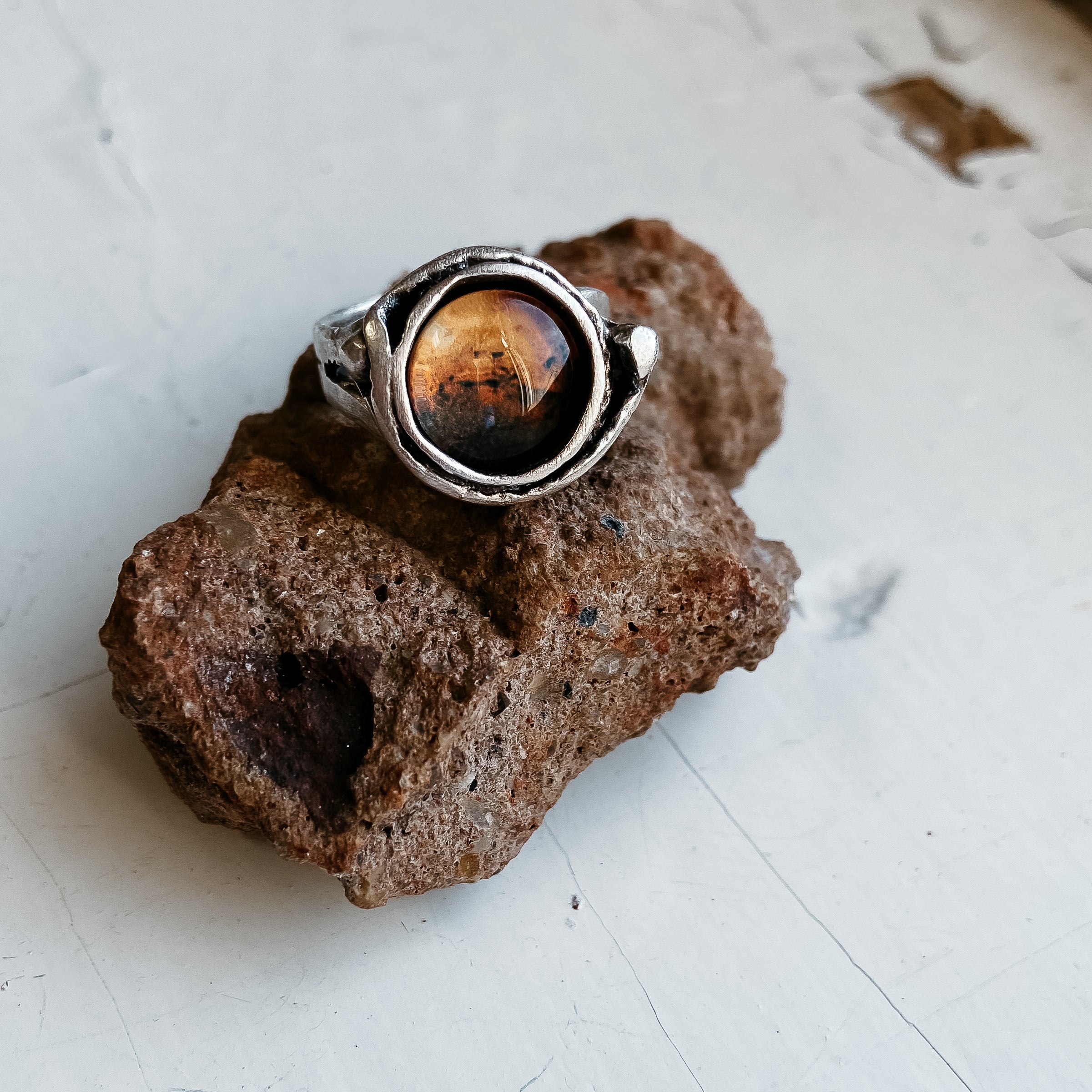 A hand wears the Mars and Moons Ring, featuring a silver tone with a spherical, galaxy-like design reminiscent of space exploration jewelry, set against a starry background.