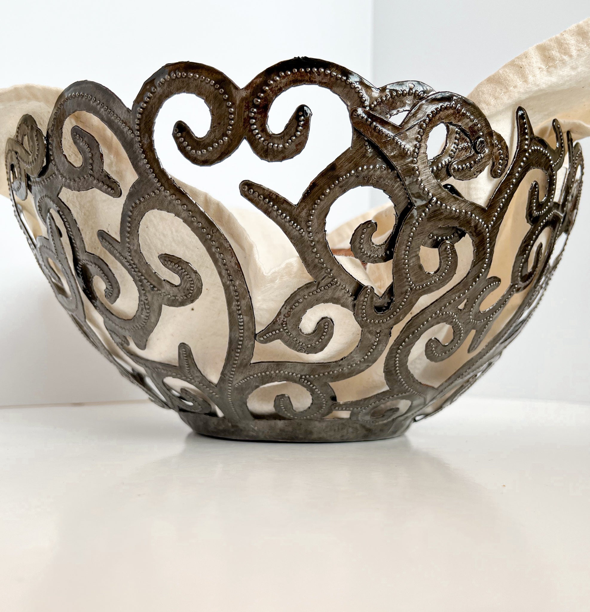 The Metal Art Scroll Bowl, intricately designed with swirling cut-out patterns and crafted from recycled steel, is elegantly displayed on a white surface.