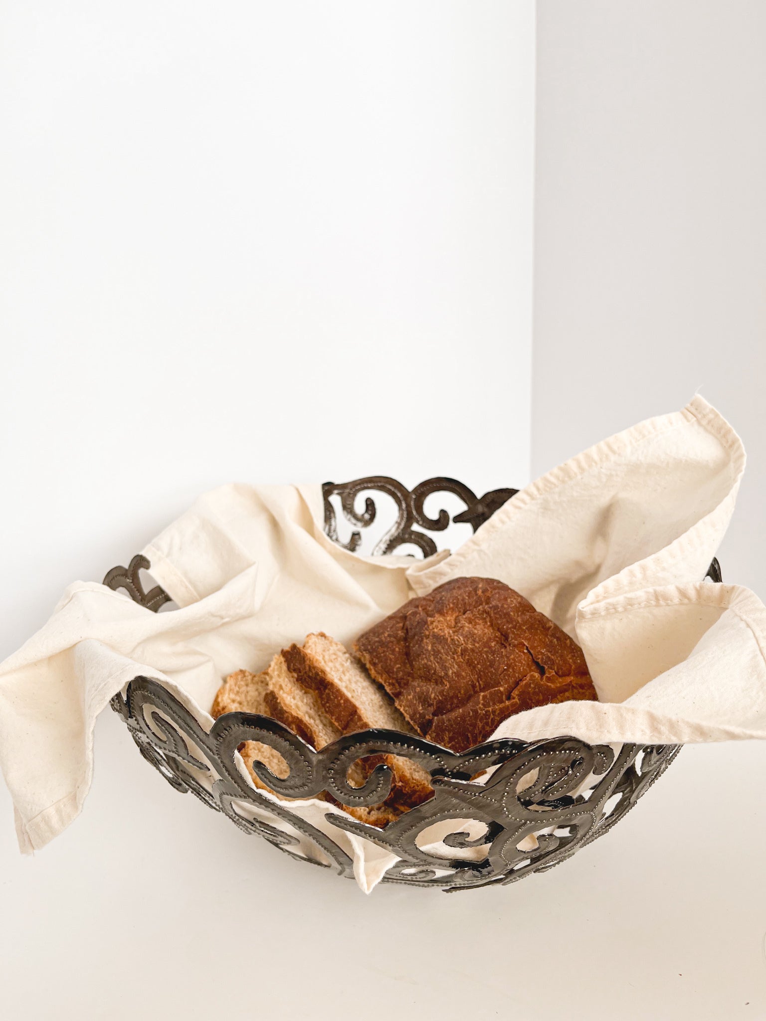 The Metal Art Scroll Bowl, intricately designed with swirling cut-out patterns and crafted from recycled steel, is elegantly displayed on a white surface.