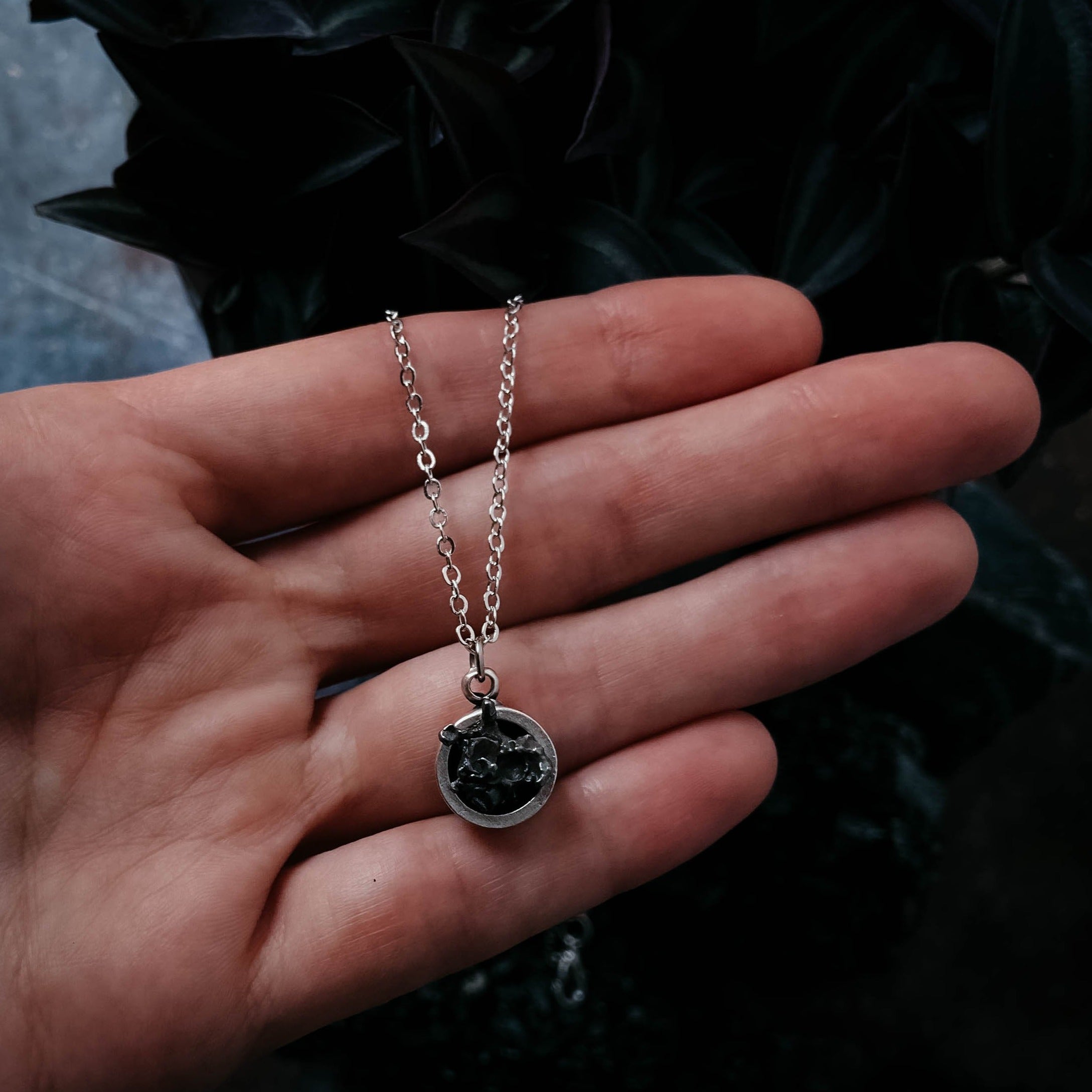 A Small Round Meteorite Pendant Necklace in Matte Brushed Silver rests on a dark background, surrounded by scattered gold and silver star-shaped decorations, embodying the enchanting allure of outer space jewelry.