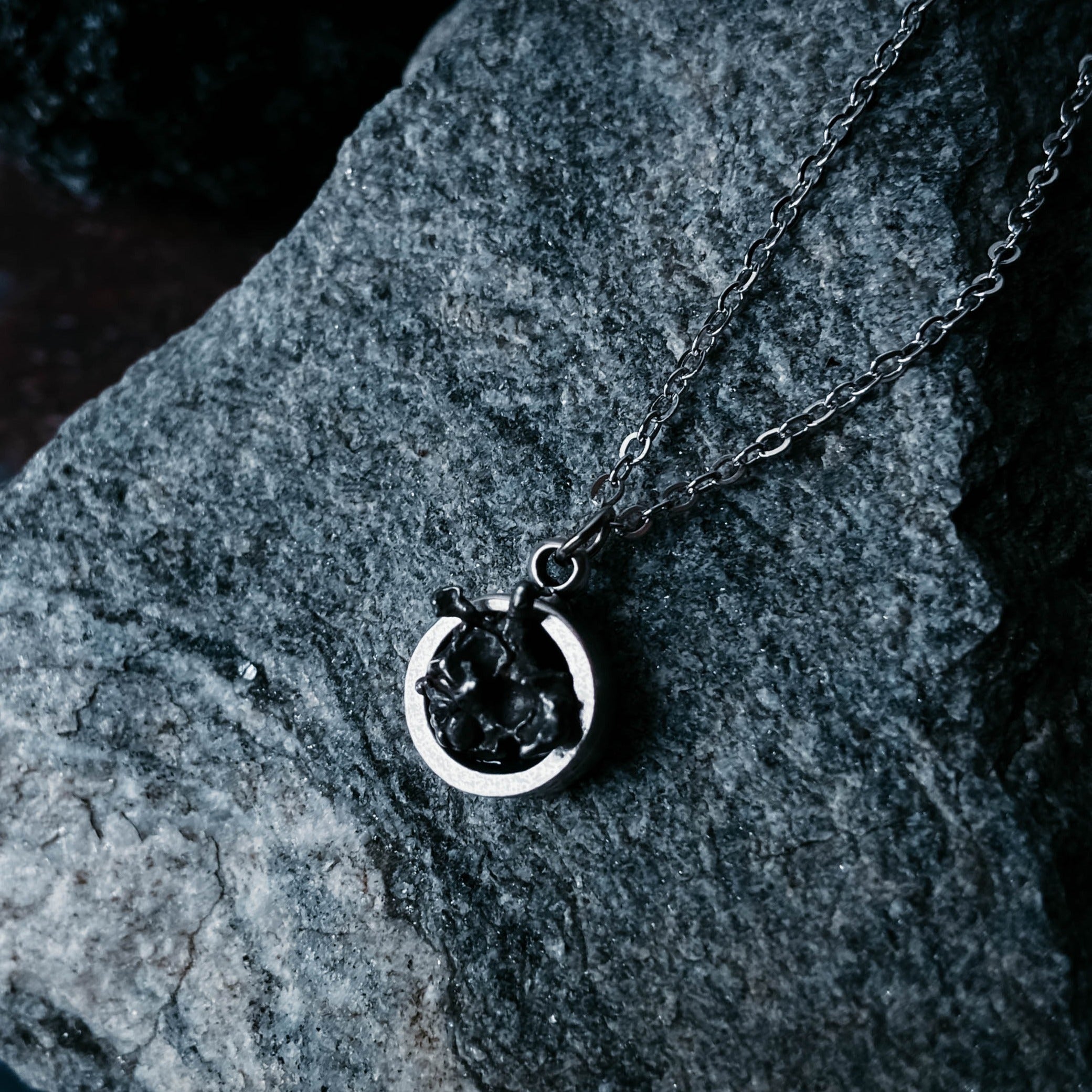 A Small Round Meteorite Pendant Necklace in Matte Brushed Silver rests on a dark background, surrounded by scattered gold and silver star-shaped decorations, embodying the enchanting allure of outer space jewelry.