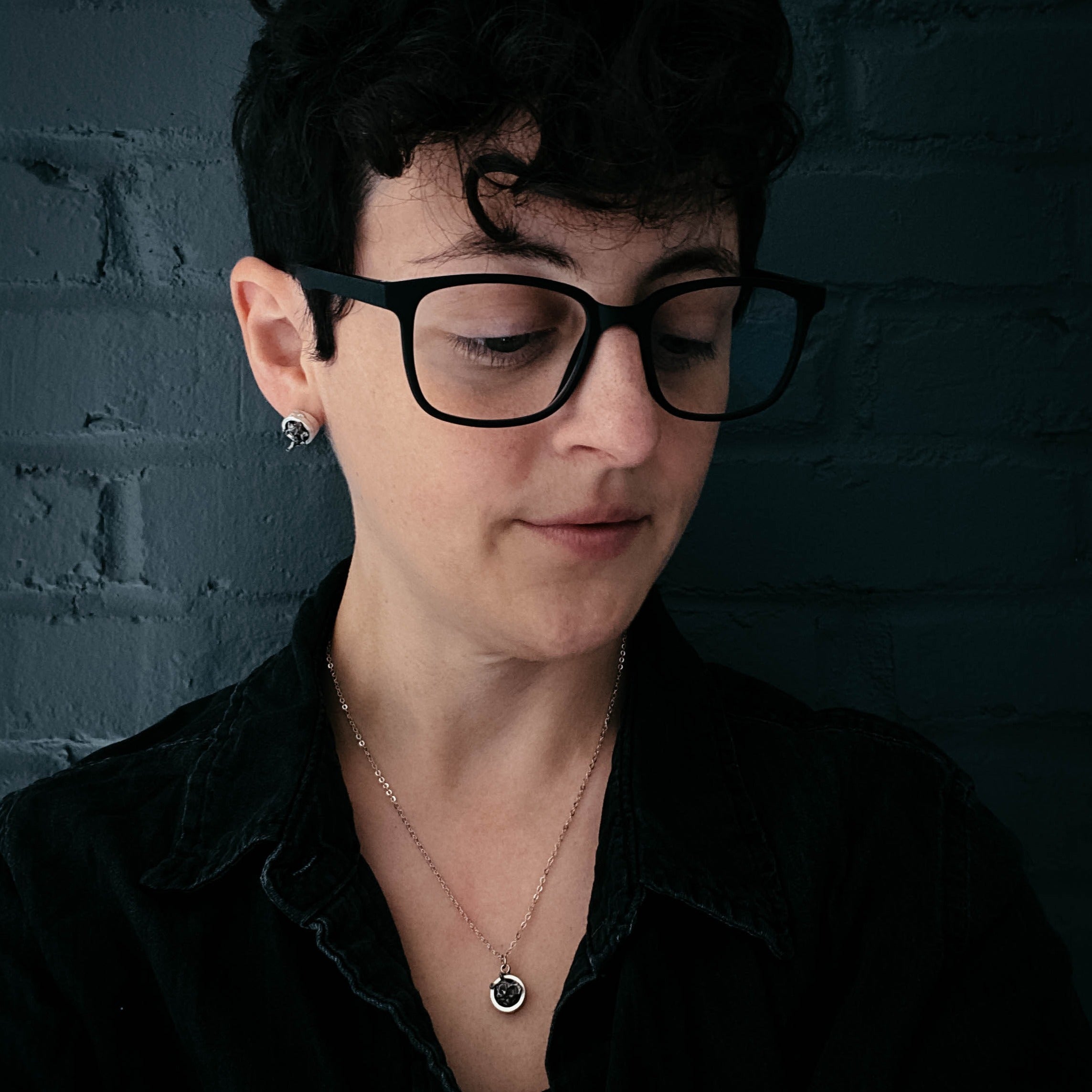 A Small Round Meteorite Pendant Necklace in Matte Brushed Silver rests on a dark background, surrounded by scattered gold and silver star-shaped decorations, embodying the enchanting allure of outer space jewelry.