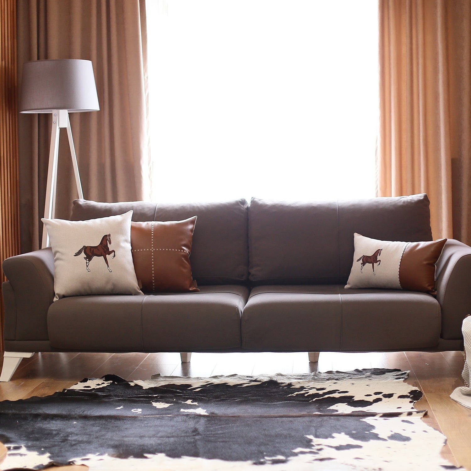 Placed on a brown sofa is the Boho Embroidered Horse Throw Pillow, a solid beige and brown square cushion measuring 18" x 18", featuring an illustration of a horse and made with recycled polyester filling, ensuring OEKO-TEX certification.