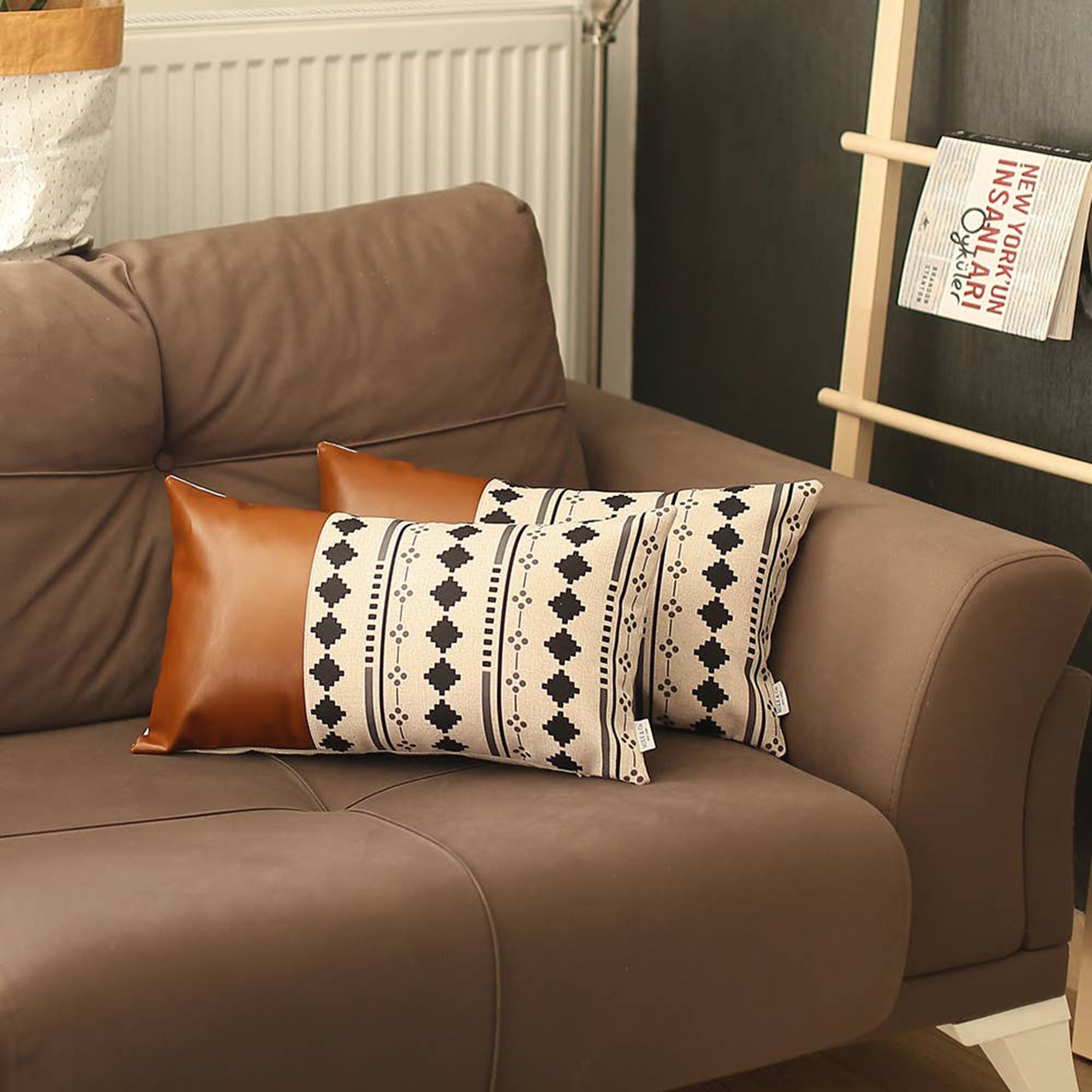 A pair of decorative pillows, featuring one in orange and another with a geometric design, are placed on a gray sofa in a modern living room. The Boho Set of 2 Handcrafted Decorative Throw Pillow Covers, made from vegan faux leather with geometric patterns, add an artistic flair that enhances the chic and cozy feel of the space.