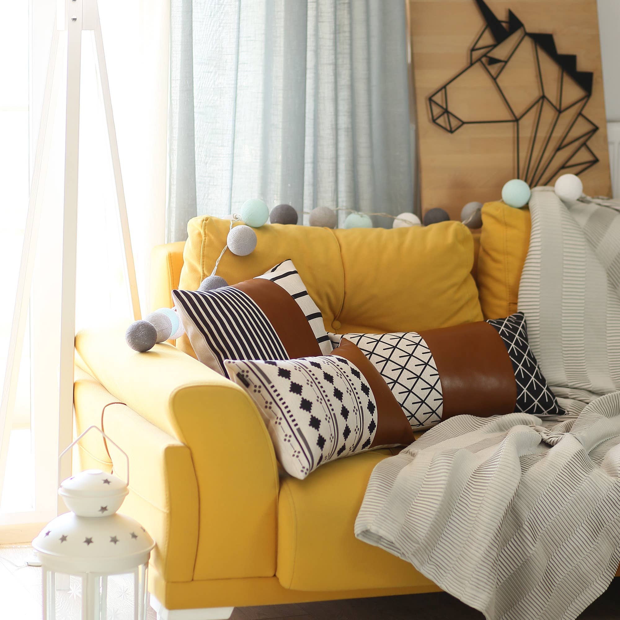 A pair of decorative pillows, featuring one in orange and another with a geometric design, are placed on a gray sofa in a modern living room. The Boho Set of 2 Handcrafted Decorative Throw Pillow Covers, made from vegan faux leather with geometric patterns, add an artistic flair that enhances the chic and cozy feel of the space.