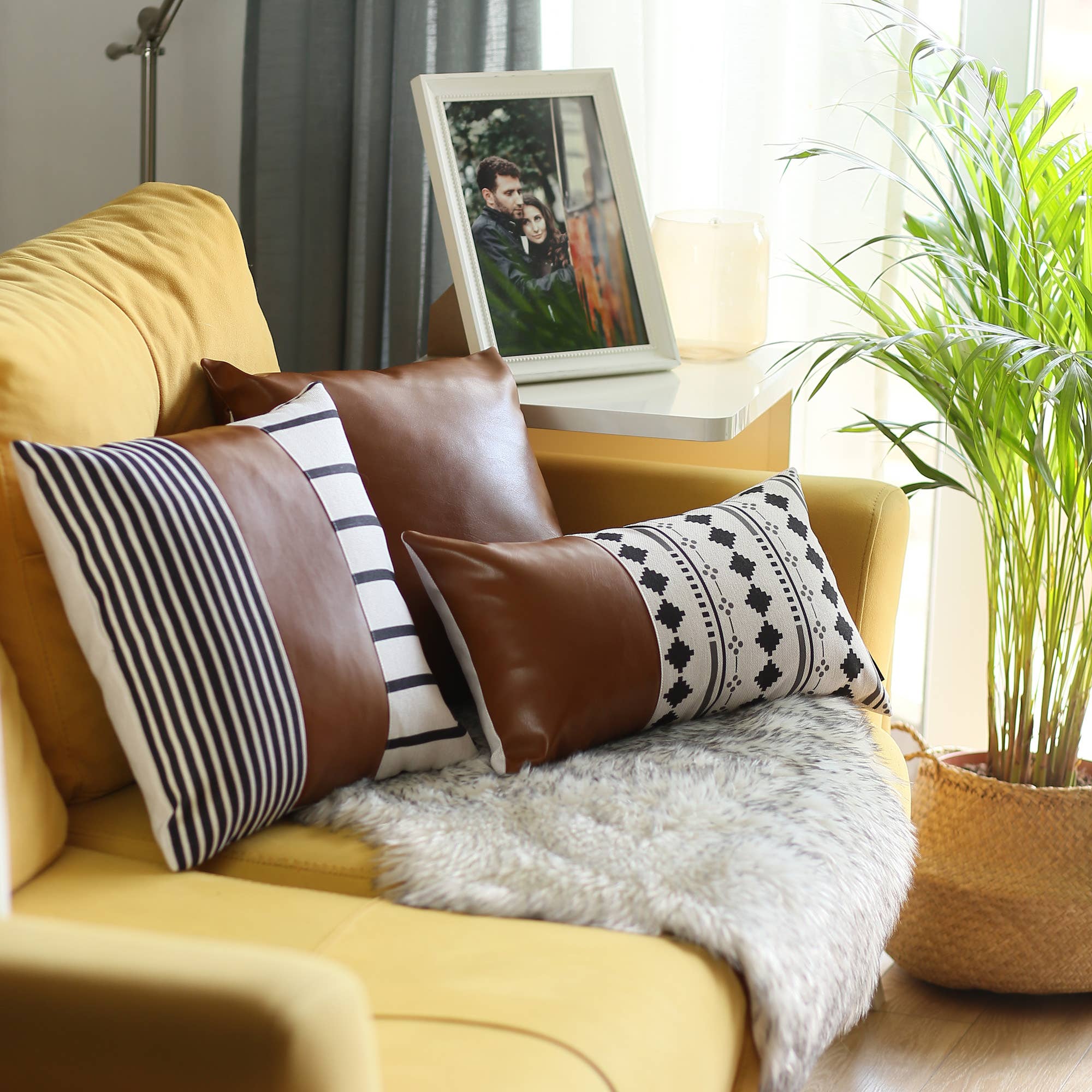 A pair of decorative pillows, featuring one in orange and another with a geometric design, are placed on a gray sofa in a modern living room. The Boho Set of 2 Handcrafted Decorative Throw Pillow Covers, made from vegan faux leather with geometric patterns, add an artistic flair that enhances the chic and cozy feel of the space.