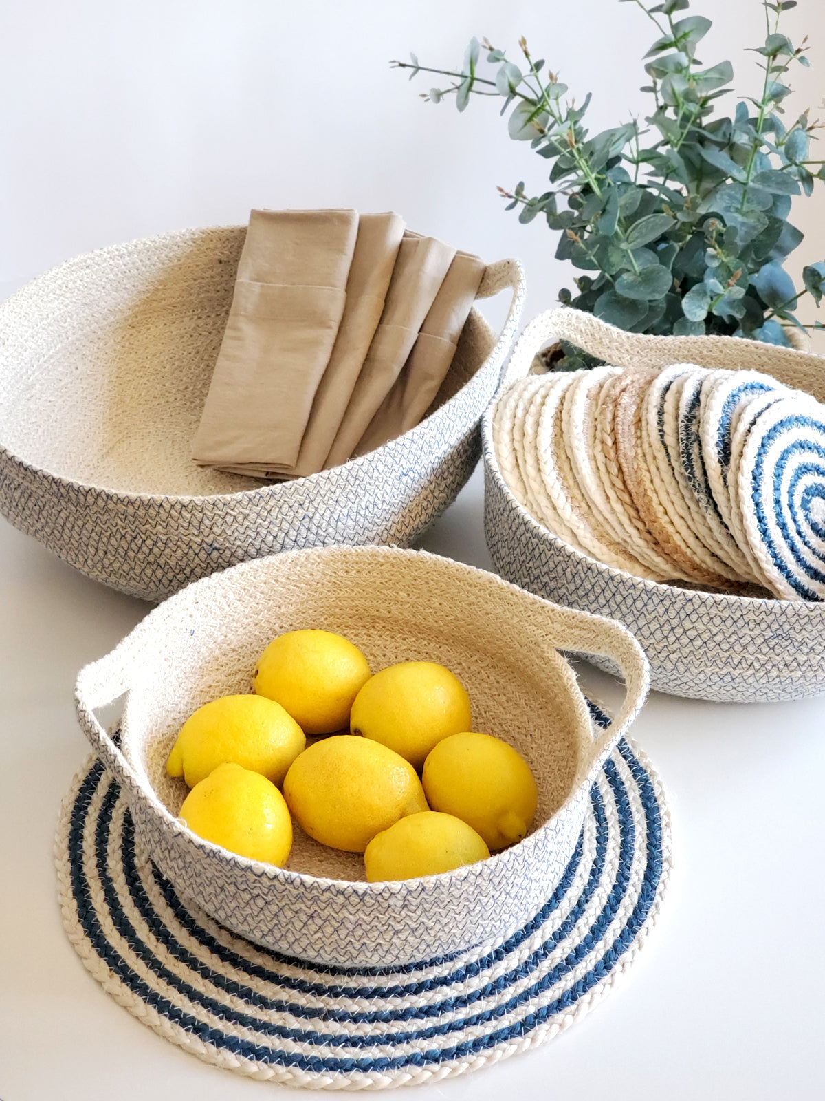 Three round, handwoven blue Amari fruit bowls are nested together. Crafted by Fair Trade artisans, these sustainably handmade pieces add a touch of elegance to any space.